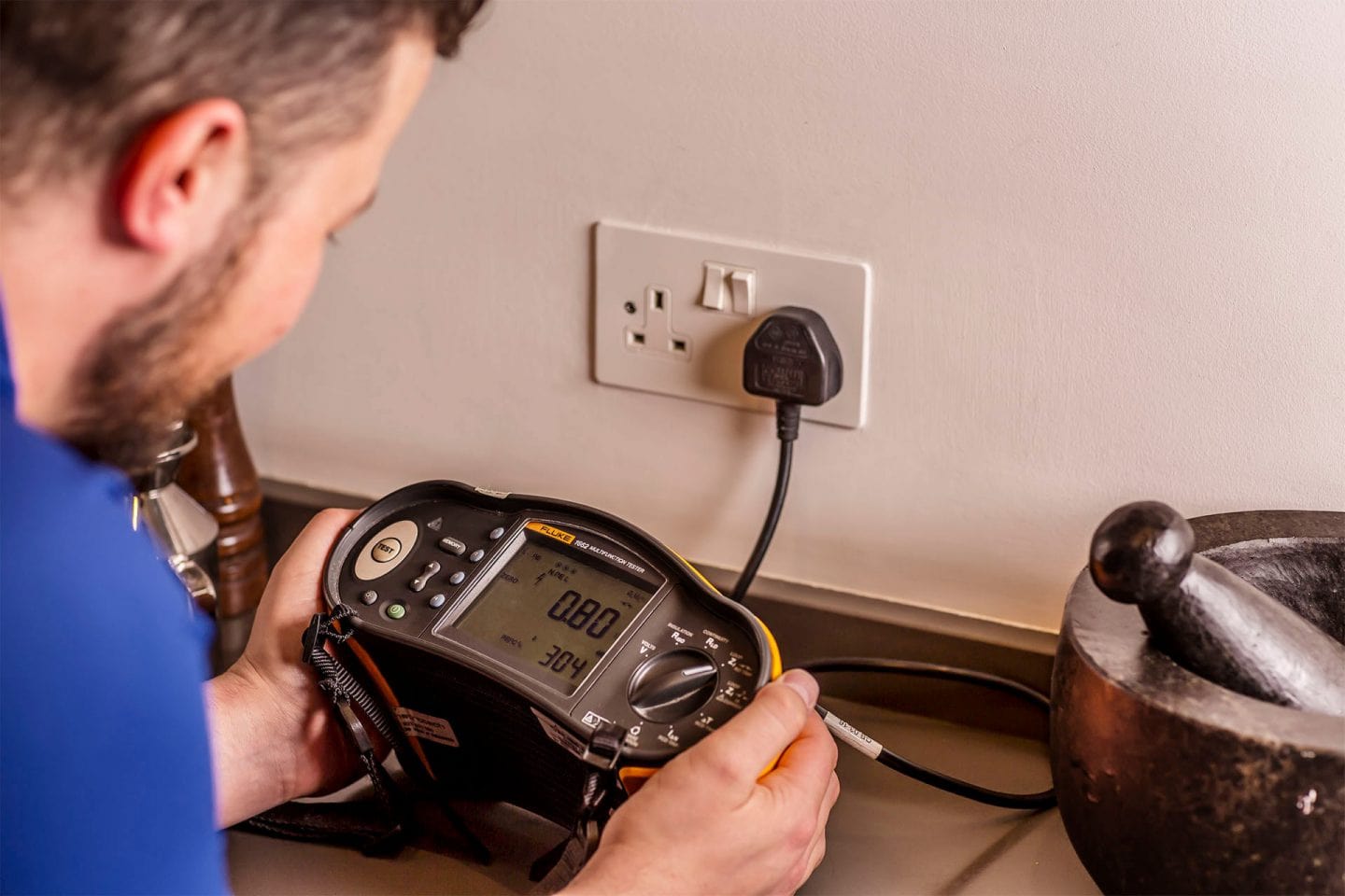 Electrician using a Fluke multifunction tester plugged into a socket to trace an electrical fault